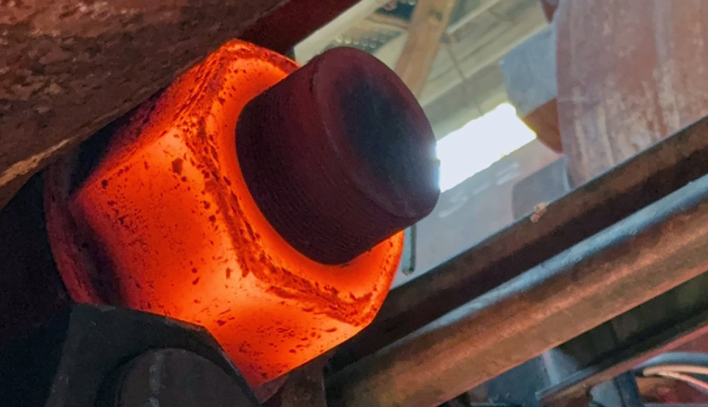 Close-up of a large industrial nut heated red-hot around a threaded bolt to facilitate bolt removal.